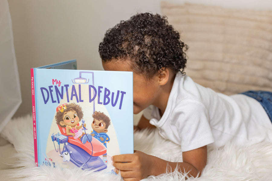 A young boy laying down on the ground and reading a book “My Dental Debut”.