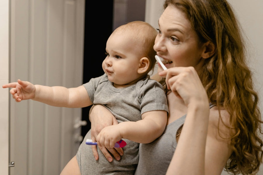 Parent holding a baby while they brush their teeth together in front of a mirror, creating a shared brushing routine. | child's first dentist visit