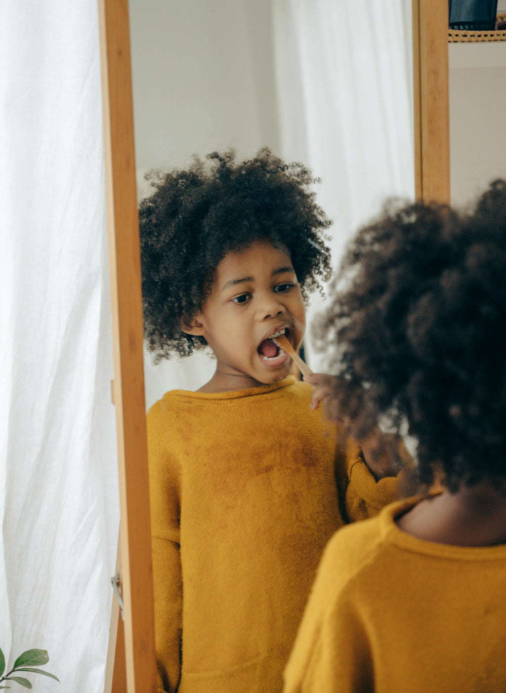A young child brushes their teeth while looking into a mirror in a softly lit bathroom. The child’s focused expression shows learning and independence, highlighting how daily brushing routines support healthy smiles at home.